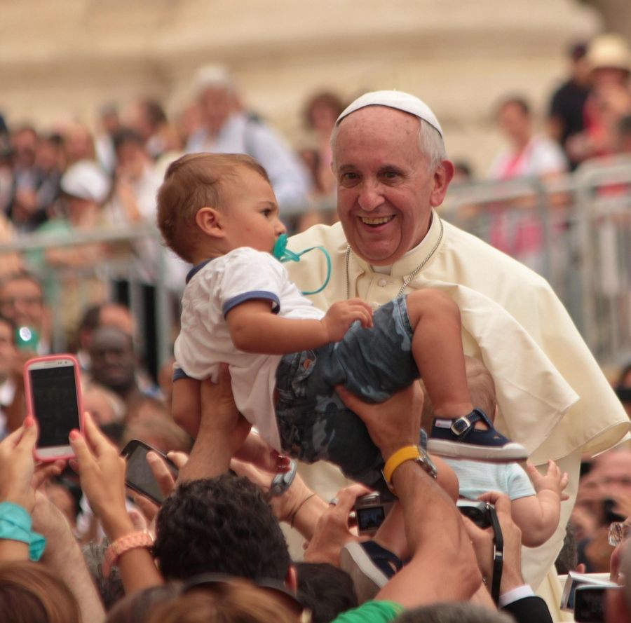 Papst Franziskus hält ein Kind im Arm
