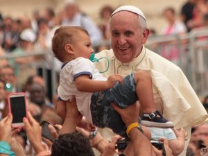 Papst Franziskus hält ein Kind im Arm